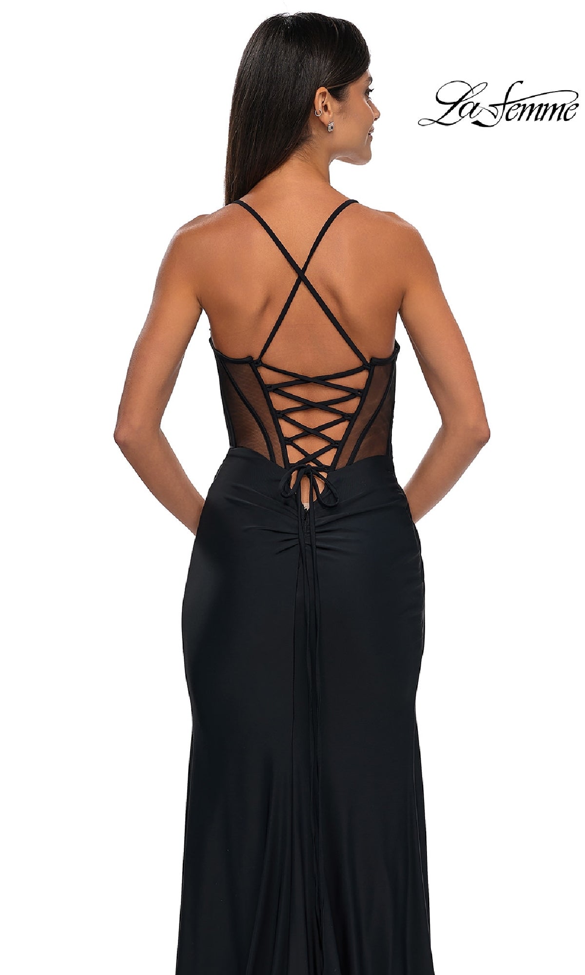A woman stands with her back to the camera in the Strappy-Back Long Black Prom Dress: La Femme 33115, featuring crisscross and lace-up back details. The